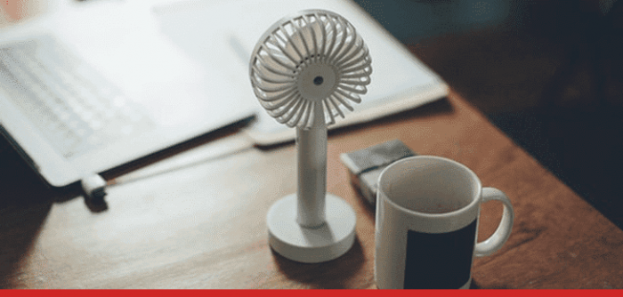 small fan and mug on a desk with a laptop to illustrate working in hot conditions