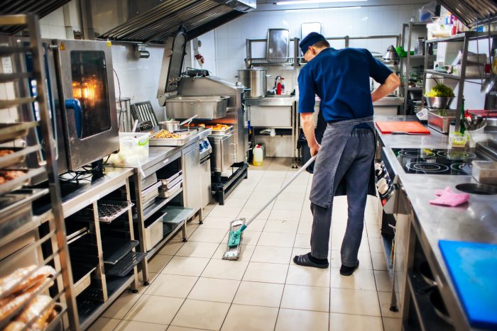 Man cleaning and sanitising floor of kitchen