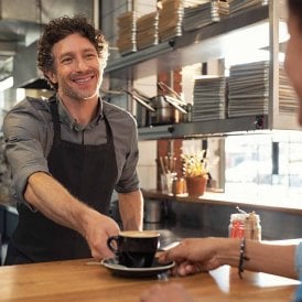 Man serving coffee with a smile, having achieved his Food Safety Level 1